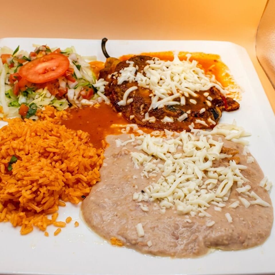 A white plate with a chile relleno, refried beans, rice, and a side salad.